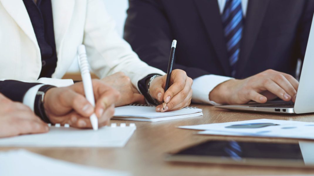 Group of business people or lawyers work together at meeting in office, hands using tablet and making notes close-up. Negotiation and communication concept